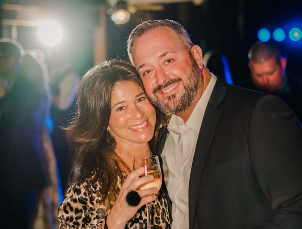 couple smiling to the camara, the woman holding a wine glass