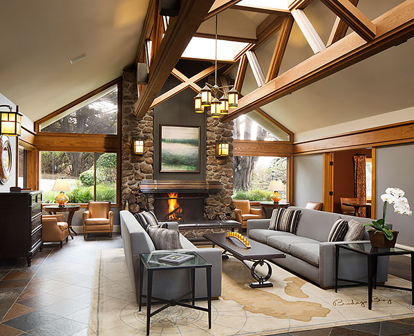Warm living space with grey couches, black table, wooden architecture ceiling & fireplace