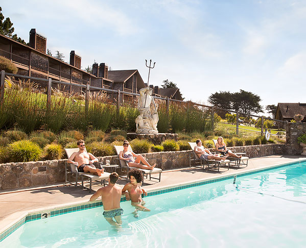 People in pool & sun bathing on loungers with property in the back