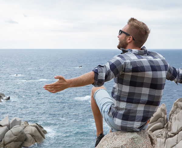 Man sitting on rock at bodega head with arms spread out wide