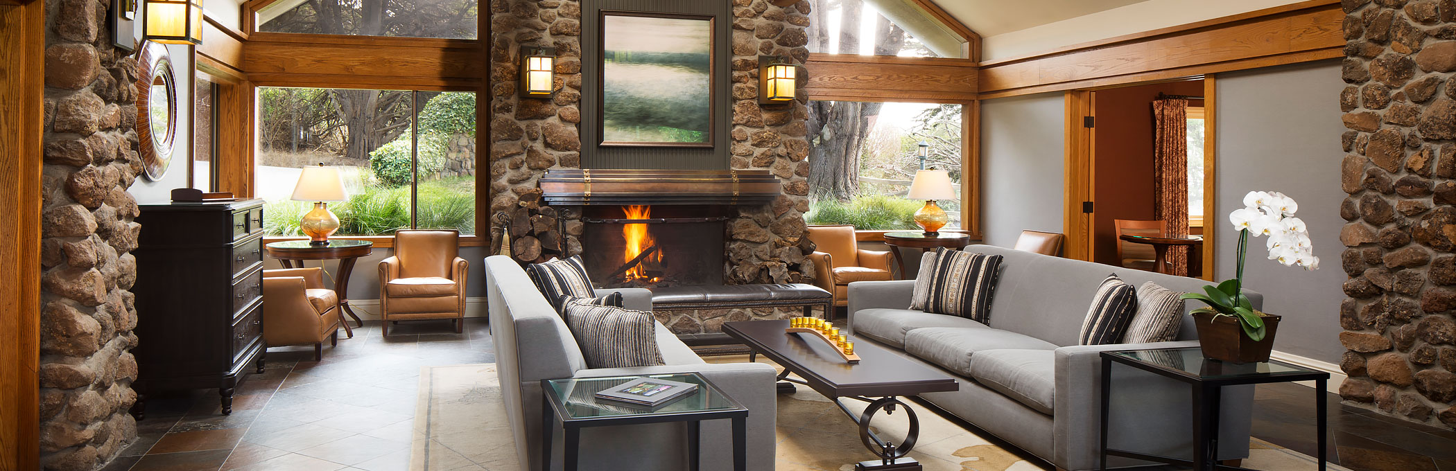Warm living space with grey couches, black table, wooden architecture ceiling & fireplace