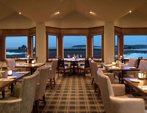 Drakes restaurant with wooden tables set for meal, sofa chairs & window panels with ocean view 
