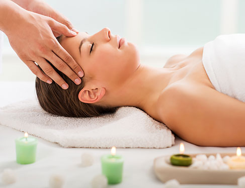 Woman on spa bed surrounded by candles getting temple massage