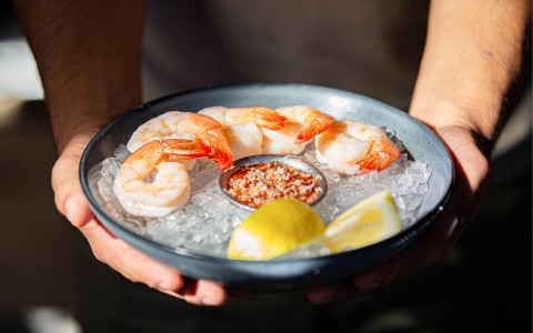 bowl of ice with shrimp and lemons on top with a side of sauce