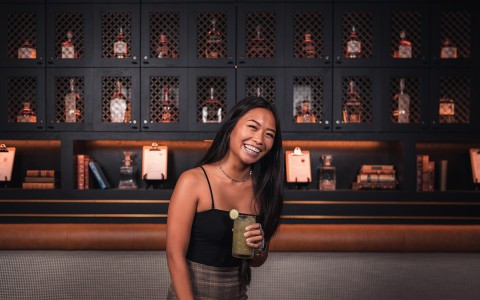 woman smiling in front of wall with whiskey bottles