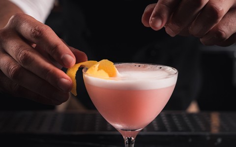 bartender adding fruit peel to pink cocktail
