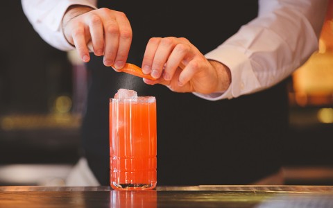 Bartender squeezing an orange peel on to an orange cocktail
