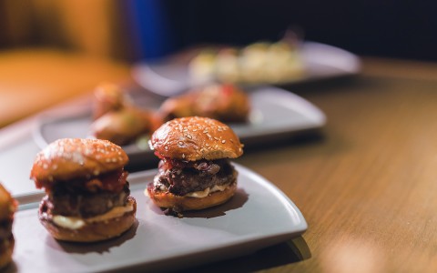 Close up of hamburger sliders with two other appetizer plates out of focus in the background