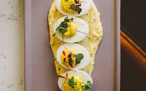 Deviled eggs atop peppercorn aioli sauce on a plate