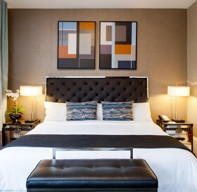 King size bed with nightstands and lamps on each side, art above the bed, window to the left and bathroom on the right
