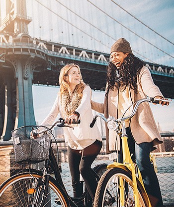 Two women riding bikes near bridge