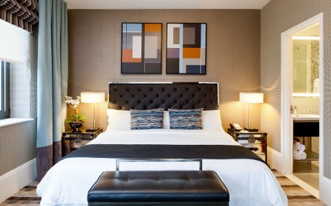 king size bed with lamps and nightstands on both sides, window, artwork above the bed, bathroom to the right 
