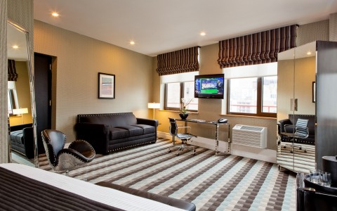 Suite with a black couch, silver studded chair, large floor length mirror, two windows, desk and chair, TV, wardrobe 