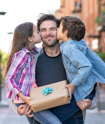 father carrying two kids with each kid kissing his cheek