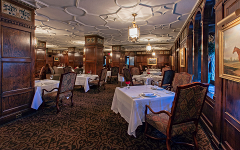 Interior view of the English Grill at The Brown Hotel with square tables, white tablecloths & dining chairs in dimly lit setting
