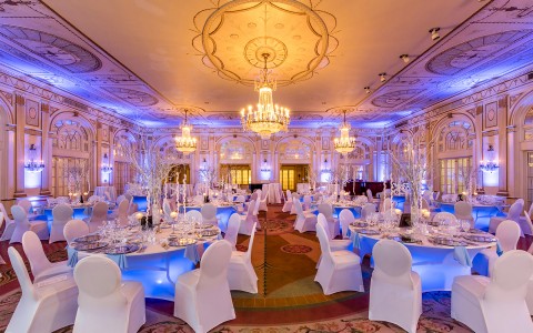 Interior view of the ballroom at our hotel in Louisville, KY outfitted with white accent chairs & tables & glass chandeliers  