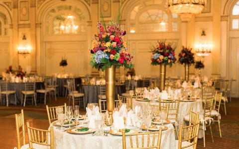 Interior view of our downtown louisville hotel wedding room. White & gold accent banquet tables, tall vases & silverware arranged at table