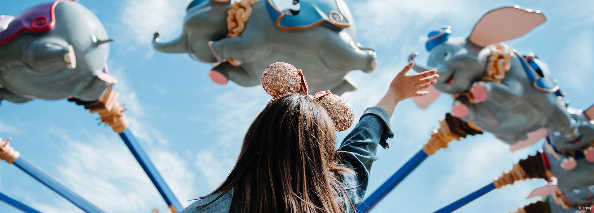 girl standing in front of the flying Dumbo ride with ears on