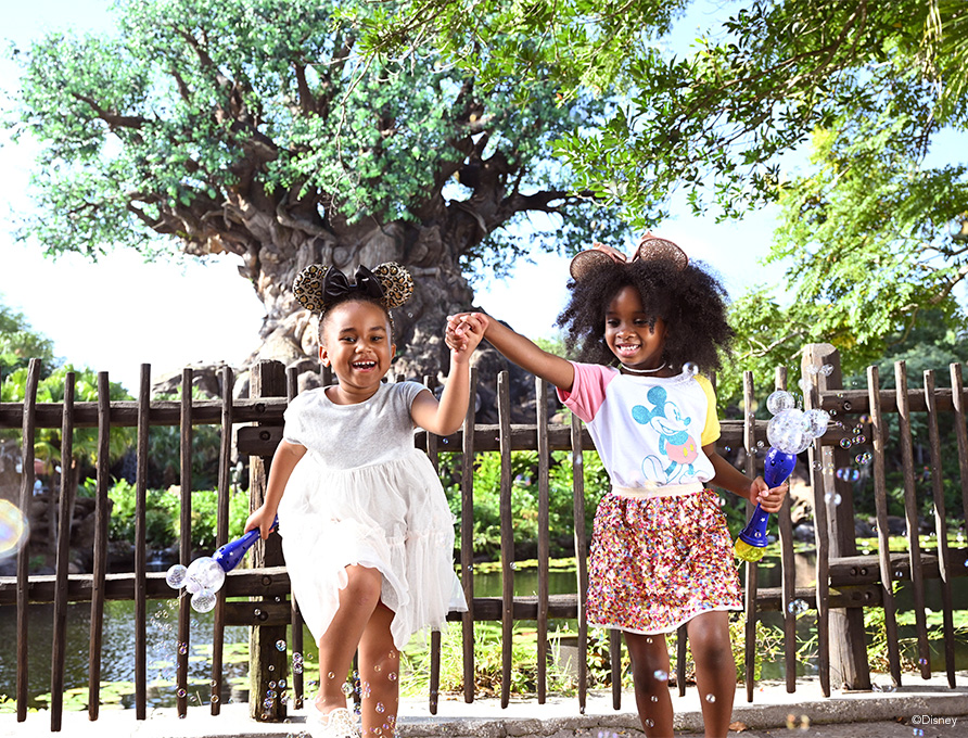 2 little girls standing in front of animal kingdom tree