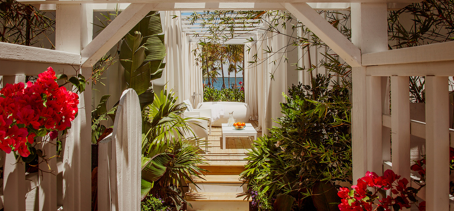 Outdoor back porch with opened white wooden fence with fuchsia flowers leading to hot tub