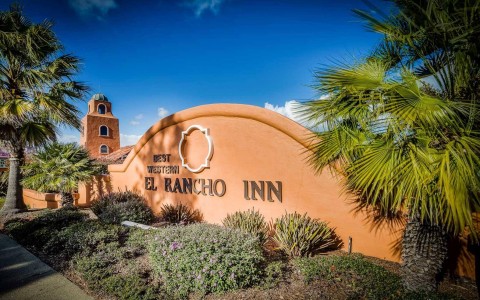 Entrance sign to the Best Western Plus El Rancho Inn surrounded by palm trees and shrubbery
