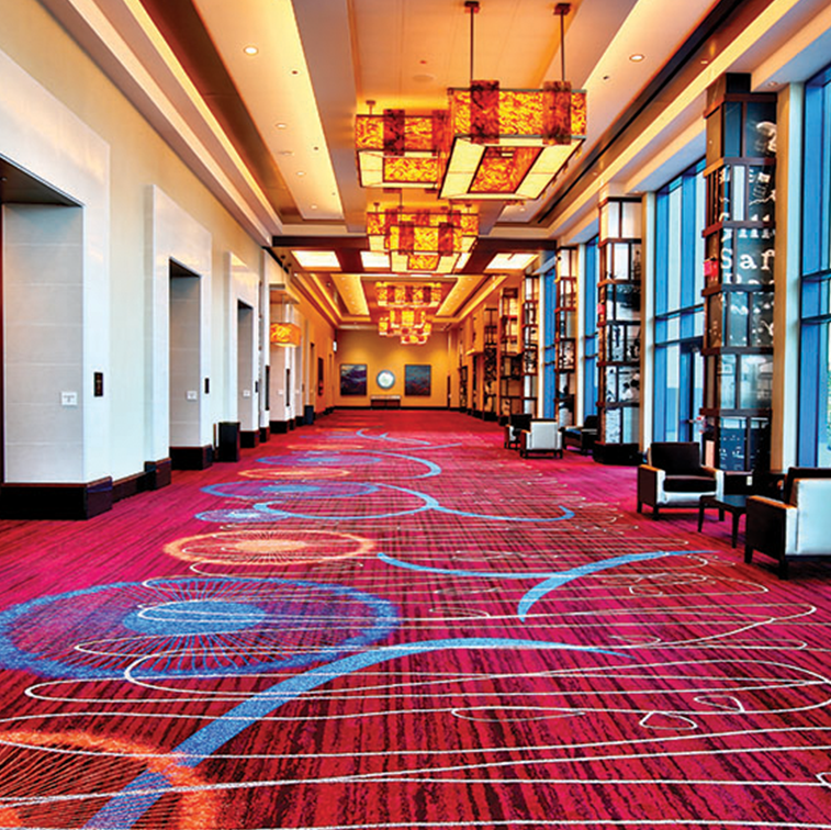A low lit corridor with bright colored carpeting and windows to the right.