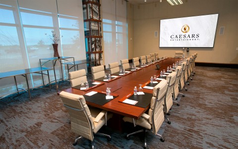 A conference room with a long oak table, chairs, and a large flat panel television.