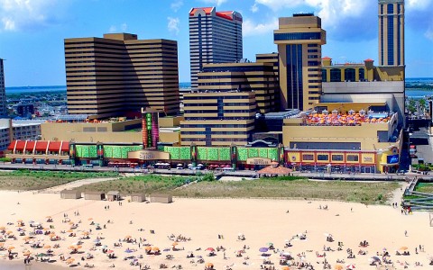 A large building next to the beach with lots of people on the sand and in the water.