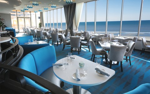 A dining room with blue bench seating and carpets overlooking the ocean.