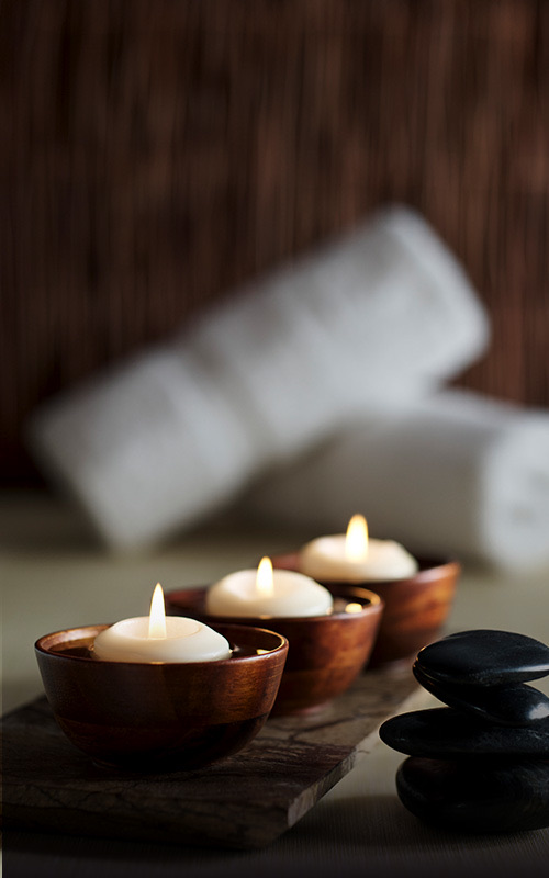 Three small tea lights with black stones stacked to the right and rolled towels in the background.