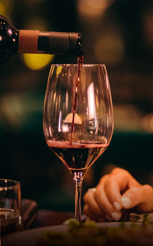 A bottle of red wine being poured into a wine glass.