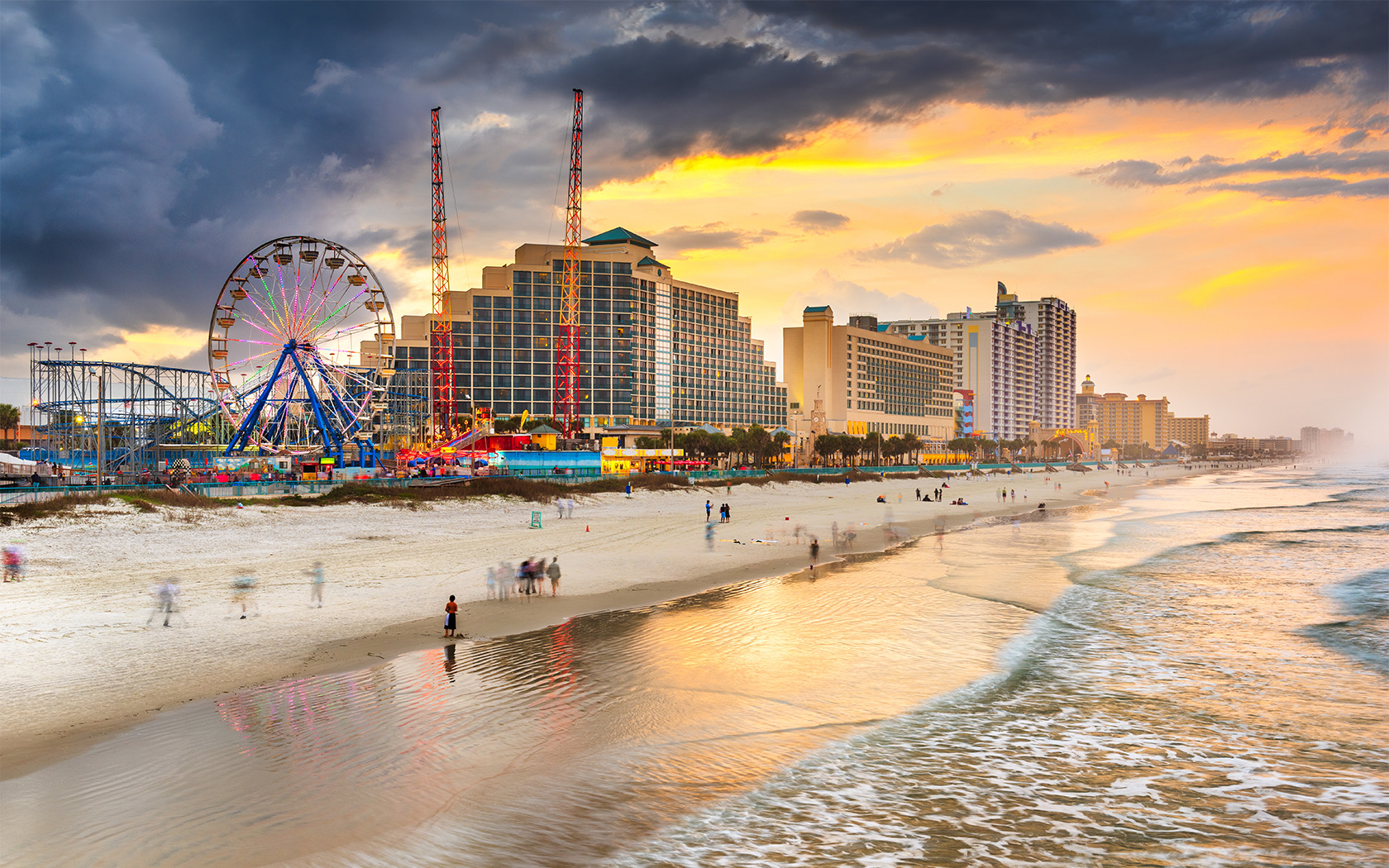 Many tall buildings and amusement rides next to the beach at sunset.