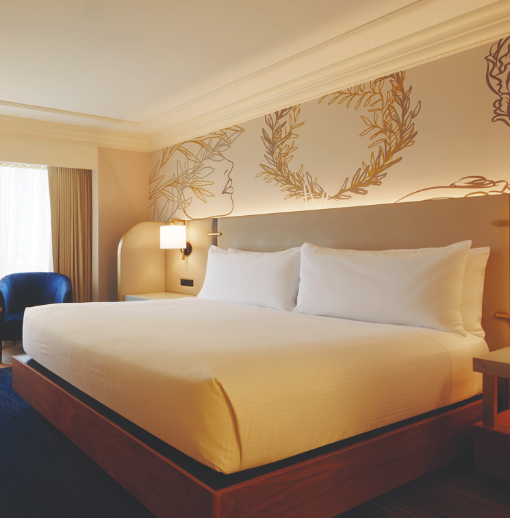 A large white bed with white and gold designed wall paper.