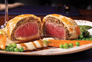 Beef wellington served with fresh peas and carrots.