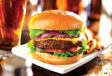 A close up of a cheeseburger with beer next to it.