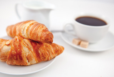 Two croissants served with a cup of coffee with cream and sugar on the side.