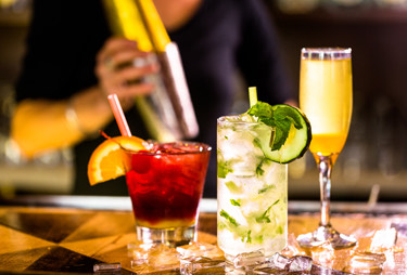Three cocktails on top of a bar with a bartender behind them.