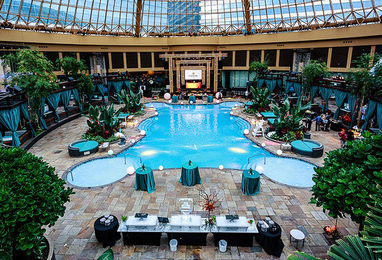 A large indoor pool with green linen high top tables and lots of plants and trees.