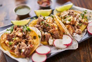 A taco platter served with sliced radishes and limes.