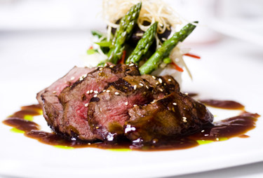 A close up of a seared filet and grilled asparagus topped with a demi glaze.