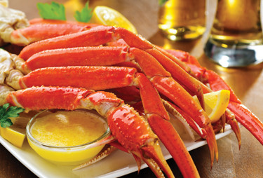 A plate of snow crab legs served with melted butter and lemon slices.