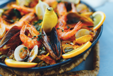 A bowl of mixed seafood over rice and served with fresh lemon wheels.