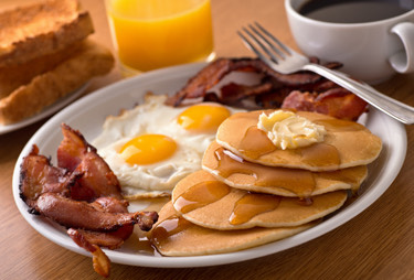 A breakfast plate with eggs, pancakes, and bacon served with a cup of coffee and orange juice.