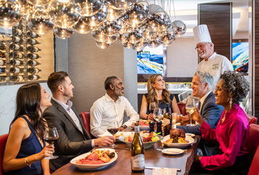 A chef talking to a group of diners at a table in the restaurant.