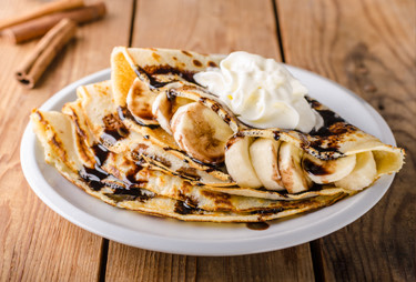 A plate of banana crepes topped with chocolate sauce and whipped cream.