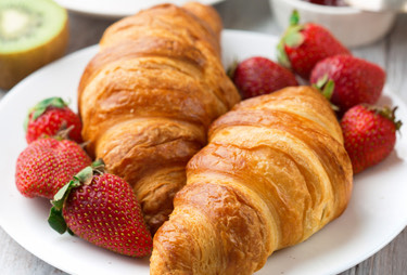 Two baked croissants served with fresh strawberries.