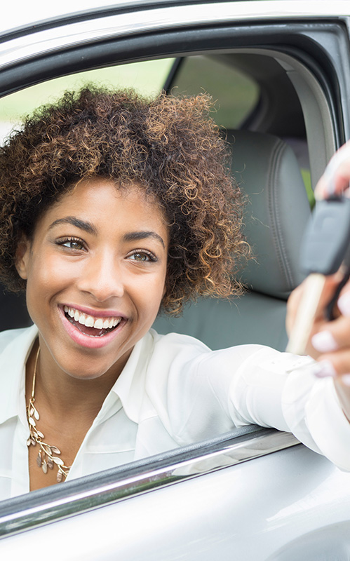 Lady with short brown hair smiling in her car while grabbing her keys from the valet.