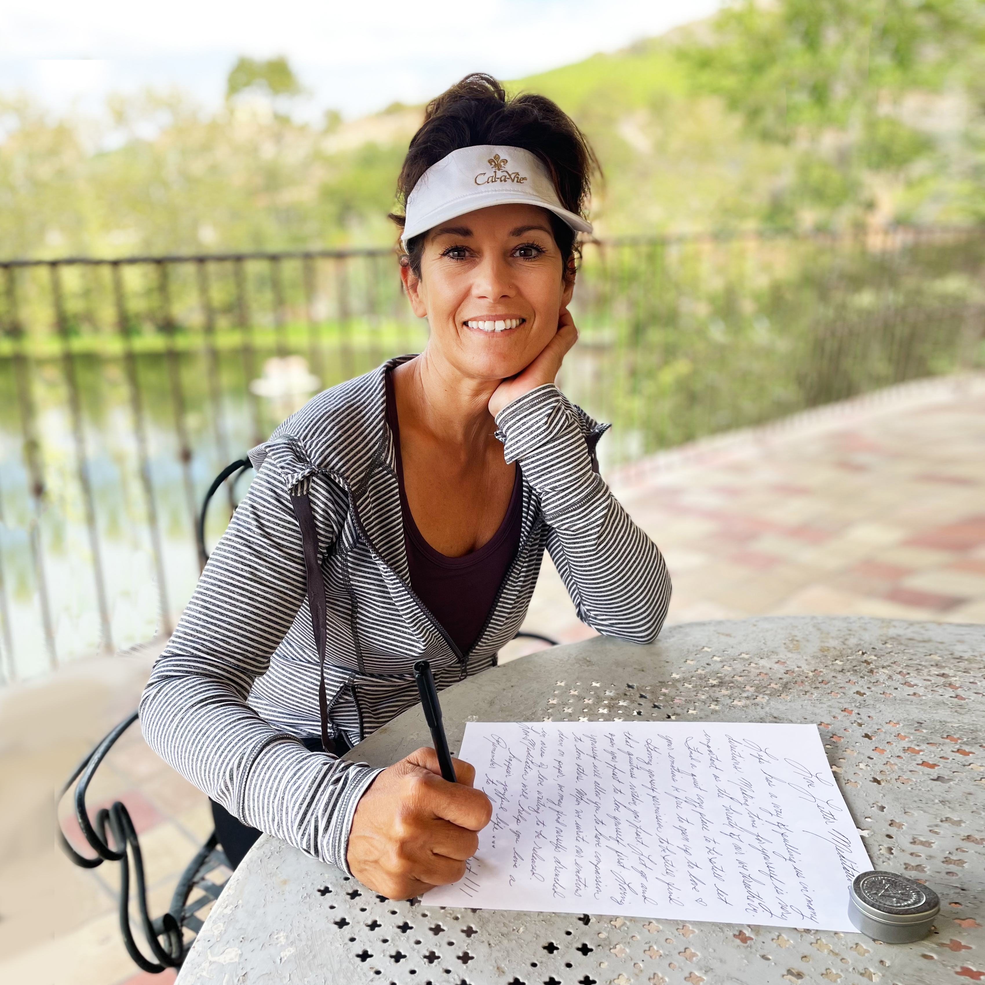 woman in visor journaling on patio table