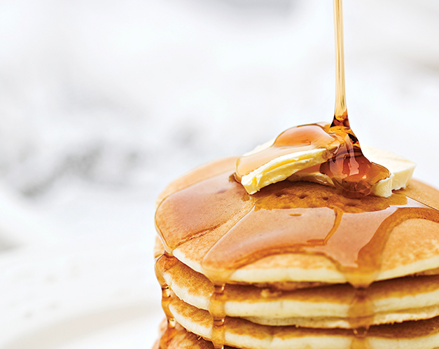 syrup being poured overtop a stack of pancakes