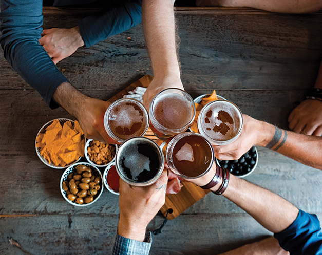 overhead view of a group of friends holding their beer glasses overtop a table for a cheers
